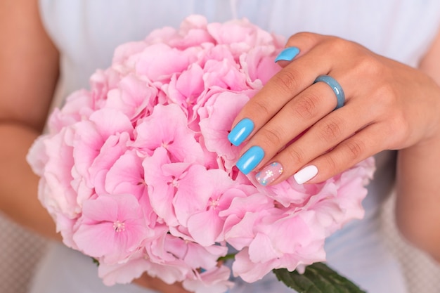 Mano femminile con unghie manicure blu che tengono fiore