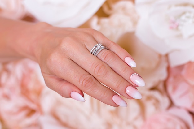 Mano femminile con unghie manicure ombre smalto gel rosa su sfondo fiori di carta