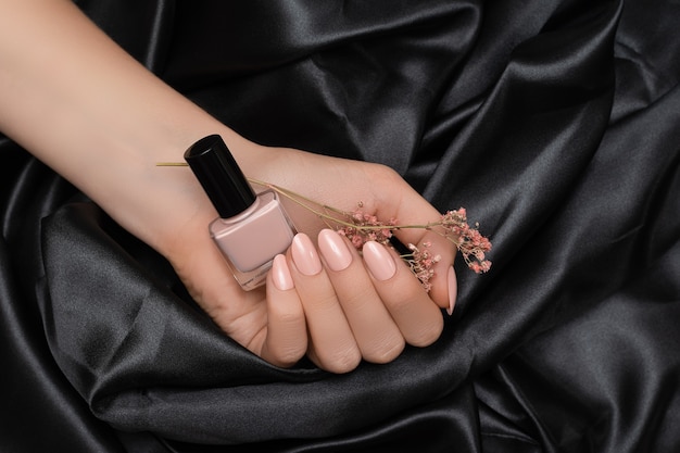 Mano femminile con unghie rosa design che tiene vernice rosso pallido su tessuto nero.