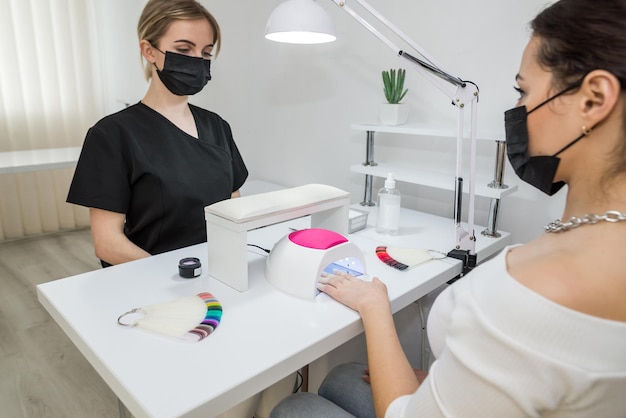 Mano femminile con unghie rosse in una lampada per manicure Manicure e cliente Una donna si asciuga le unghie in una lampadaUna lampada per asciuga unghie per asciugare lo smalto gel Cura delle unghie