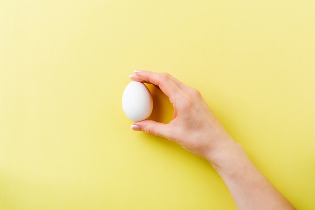 Mano femminile con uovo di gallina crudo bianco che si trova sulla luce gialla