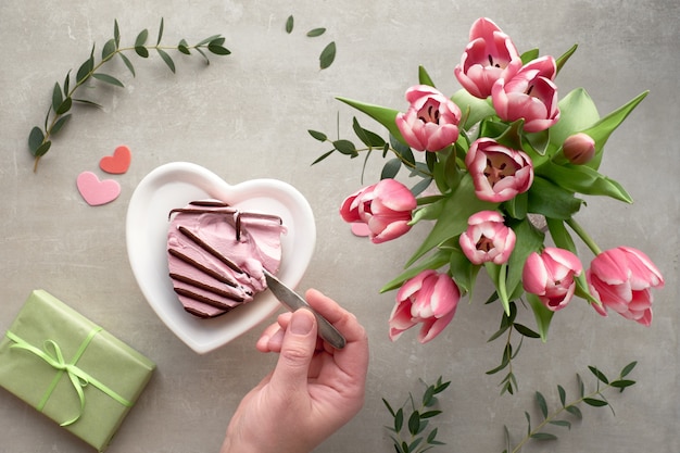 Mano femminile immergendo un cucchiaio nel gelato cuore rosa e tulipani rosa