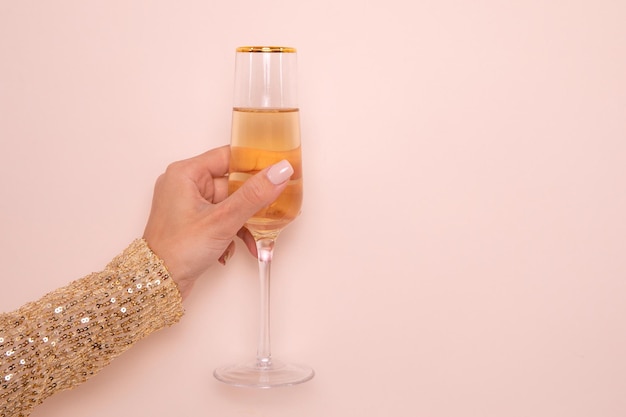 Mano femminile in abito dorato che tiene un bicchiere di champagne su fondo beige