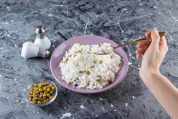 Mano femminile prendendo delizioso riso con forchetta su sfondo marmo.