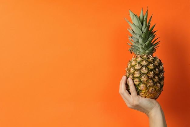 Mano femminile tenere ananas maturo su sfondo arancione