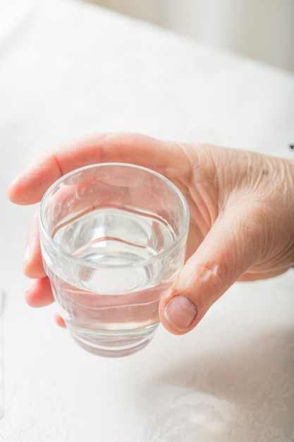 Mano femminile tenere il bicchiere d'acqua. Assistenza sanitaria e medica per anziani. Medicinali per il trattamento di anziani.