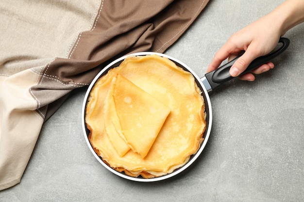 Mano femminile tenere padella con frittelle sottili sul tavolo grigio