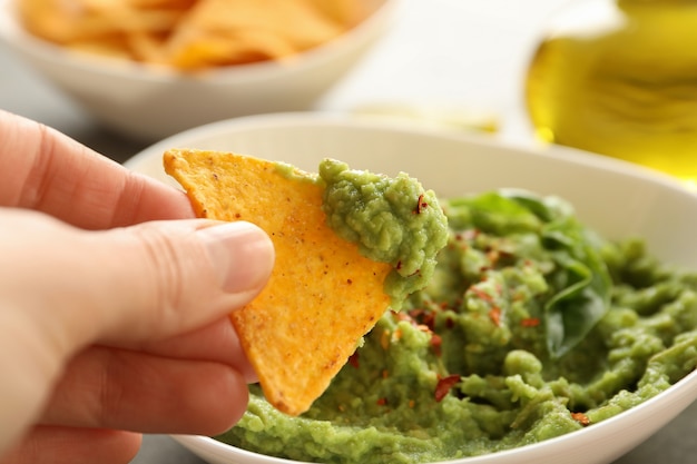 Mano femminile tuffi patatine fetta in guacamole, primi piani