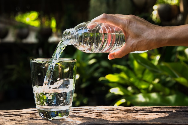 Mano femminile versando acqua dalla bottiglia al vetro sullo sfondo della natura