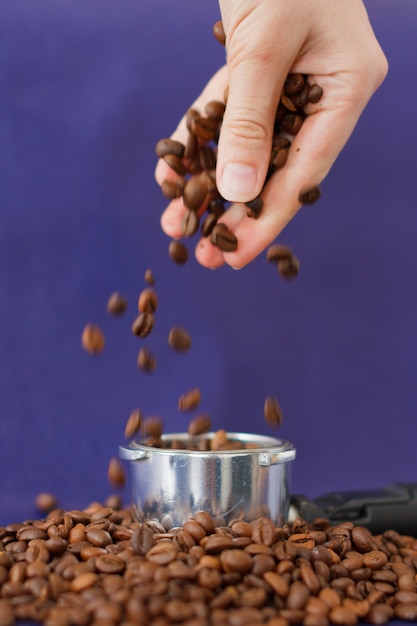 Mano femminile Versando i chicchi di caffè nel tamper del caffè sulla superficie viola