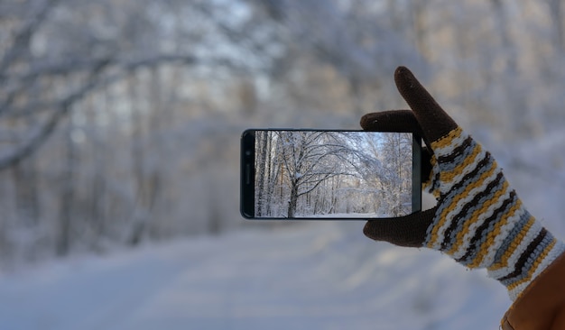 Mano in guanto di lana che tiene smartphone e scatta foto di un bellissimo paesaggio invernale