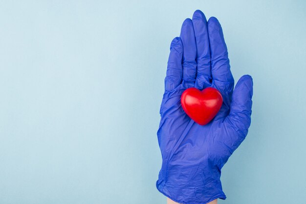 Mano in guanto medico che tiene piccolo cuore rosso