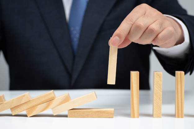 Mano maschile che ferma l'effetto domino. Concetto di controllo del rischio.