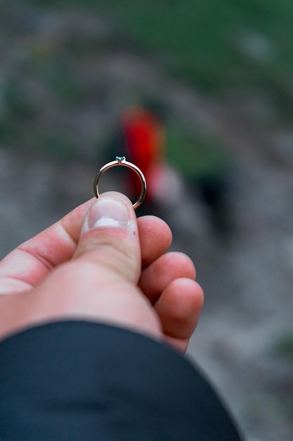 Mano maschile che tiene un anello su uno sfondo sfocato di una proposta di matrimonio donna