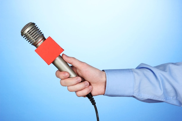 Mano maschile con microfono su sfondo blu