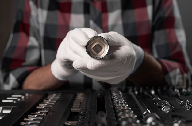 Mano maschile in guanti da costruzione bianchi con presa esagonale in acciaio metallico, testa esagonale in metallo. Strumento di riparazione auto in metallo, primo piano.