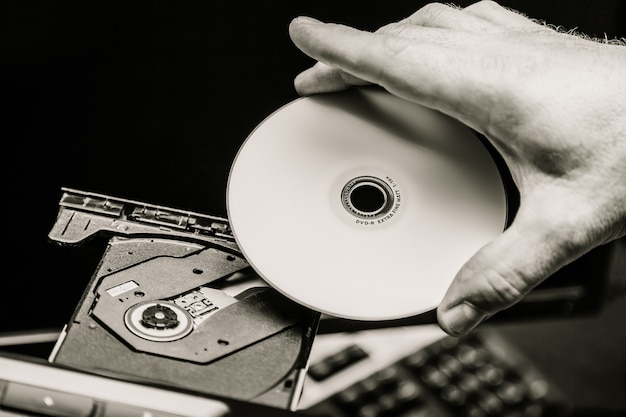 Mano maschio che inserisce un DVD in un'unità disco. Bianco e nero