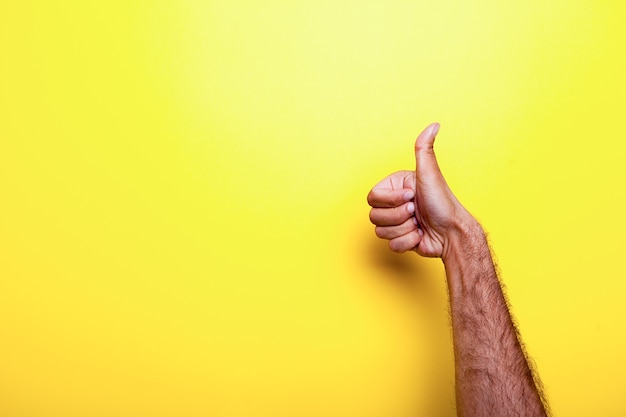 Mano maschio che mostra un pollice in alto segno su sfondo giallo. Foto in studio