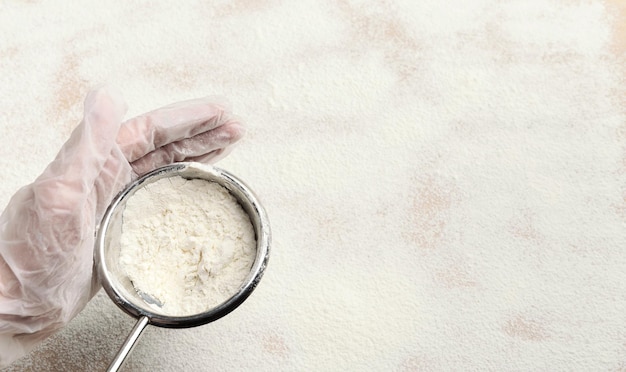 Mano maschio che setaccia la farina dal setaccio sul tavolo da cucina bianco. Processo di cottura della pasticceria