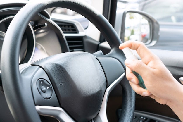 Mano maschio che spruzza alcol al volante dell'auto per la disinfezione.