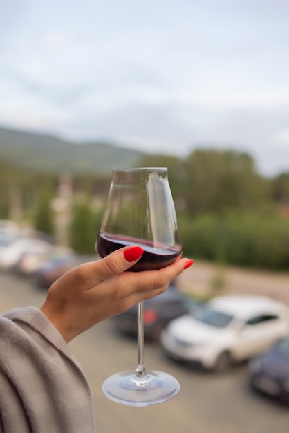 Mano maschio che tiene il bicchiere con vino su sfondo naturale sfocato.