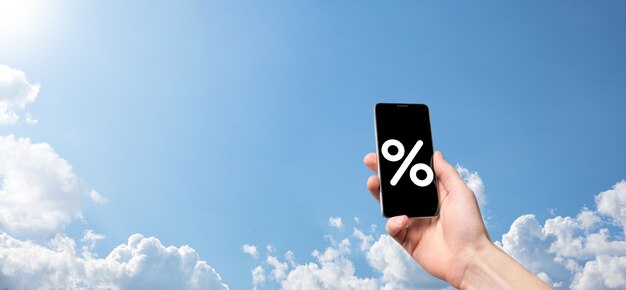 Mano maschio che tiene l'icona percentuale del tasso di interesse sullo sfondo del cielo blu. Tasso di interesse finanziario e concetto di tassi ipotecari. Banner con spazio di copia