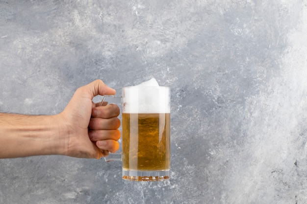 Mano maschio che tiene la tazza di birra spumosa fredda sulla superficie di marmo.