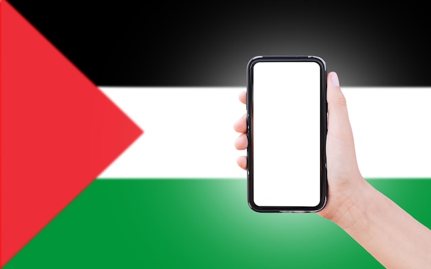 Mano maschio che tiene smartphone con spazio vuoto sullo schermo sullo sfondo della bandiera sfocata della Palestina Vista in primo piano