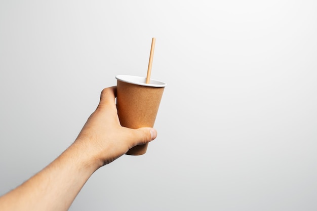 Mano maschio che tiene tazza di caffè di carta con paglia di bambù su bianco