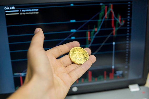 Mano maschio dell'uomo d'affari che tiene bitcoin su uno sfondo di grafico di crescita su uno schermo