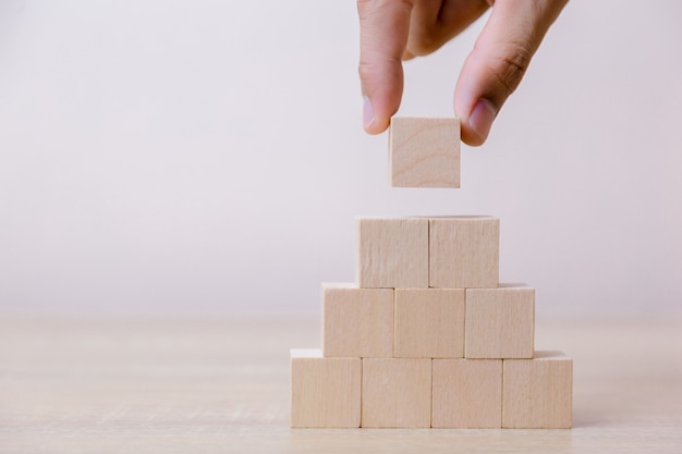 Mano mettendo blocco cubo di legno sulla piramide superiore.