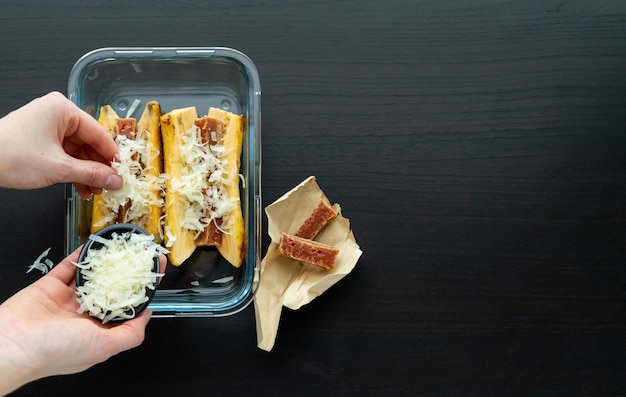 Mano mettendo il formaggio per cucinare Banane mature al forno con guava e panino al formaggio su una base di legno nera