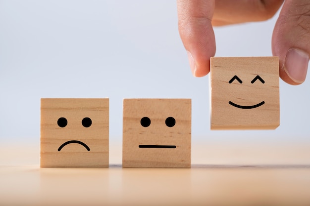 Mano mettendo l'emozione di smiley tra l'emozione normale e triste che stampa schermo su cubi di legno. Sondaggio sull'esperienza del cliente e concetto di feedback sulla soddisfazione.