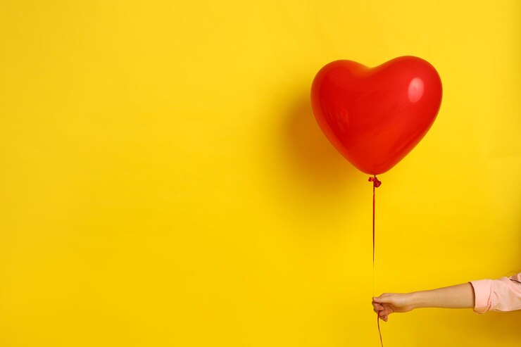 Mano nella mano in una camicia rosa tiene una palla a forma di cuore su uno sfondo giallo Immagine per San Valentino