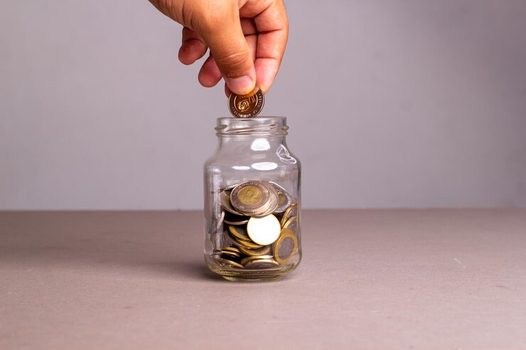 Mano pone dinero en monedas dominicanas en un frasco de vidrio "ahorros".