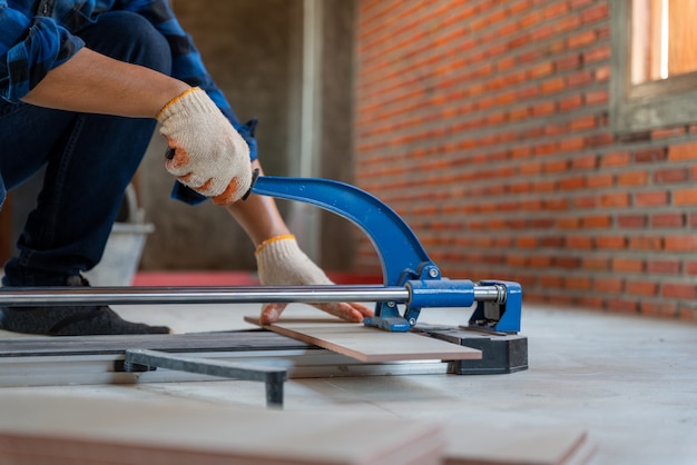 Mano ravvicinata di un piastrellista artigianale in cantiere, il lavoratore taglia una grande lastra di piastrelle durante la costruzione di una casa.