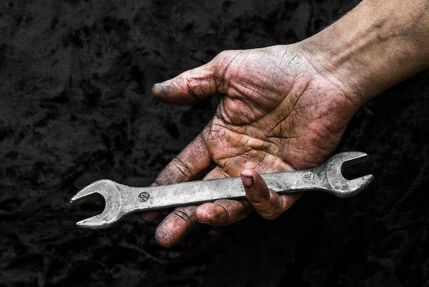 Mano sporca del lavoratore con la chiave inglese nell'officina di riparazione dell'automobile