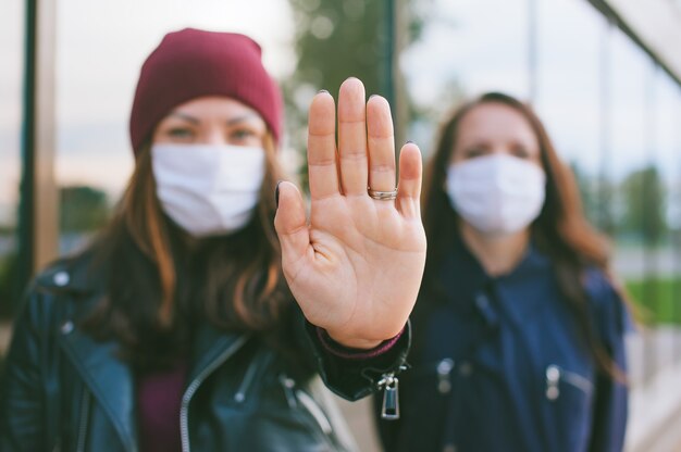 Mano sul primo piano della macchina fotografica, femmina in maschere mediche. Sullo sfondo di un edificio di vetro. Concetto di arresto del virus.