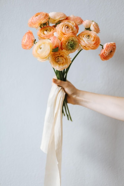 Mano tagliata che tiene fiori d'arancia vicino a una parete bianca