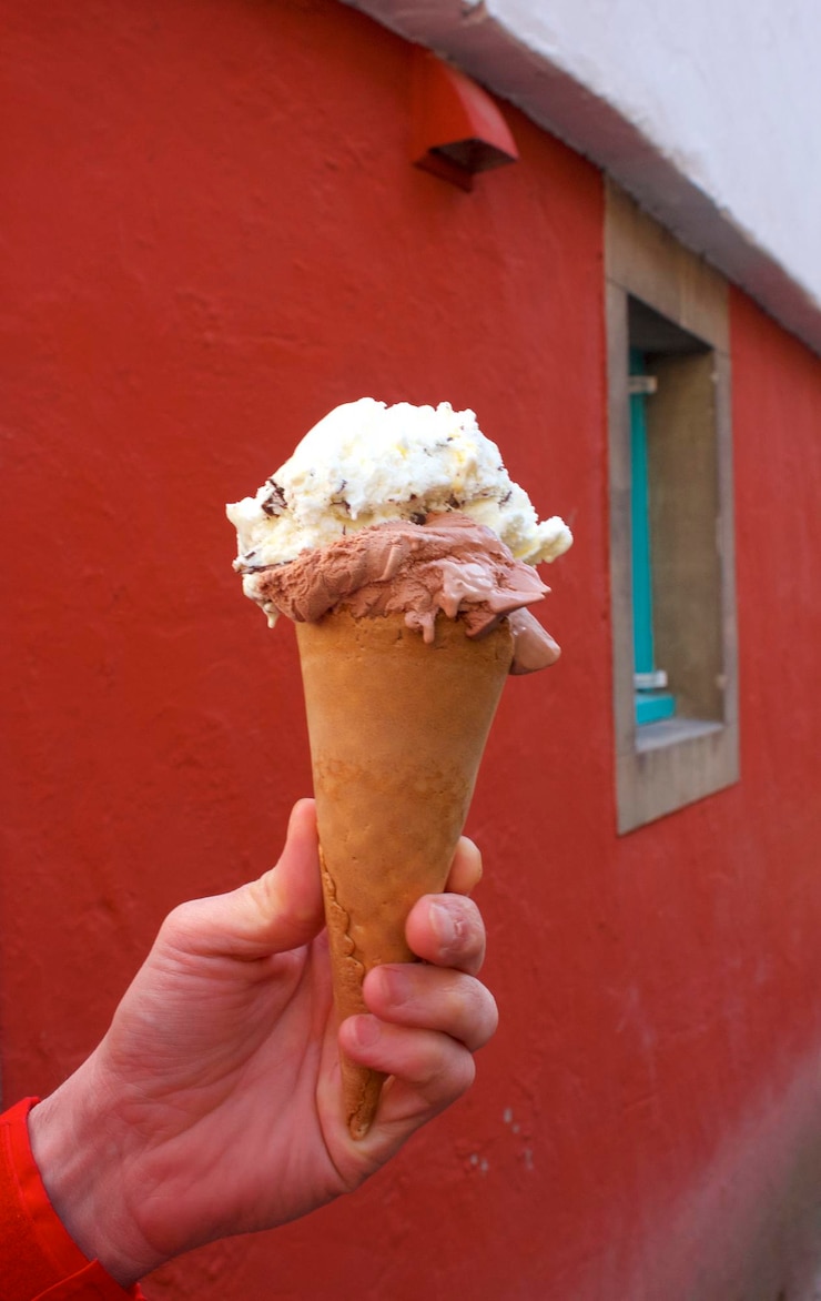 Foto mano tagliata che tiene il gelato contro la parete rossa