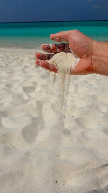 Mano tagliata che tiene la sabbia sulla spiaggia