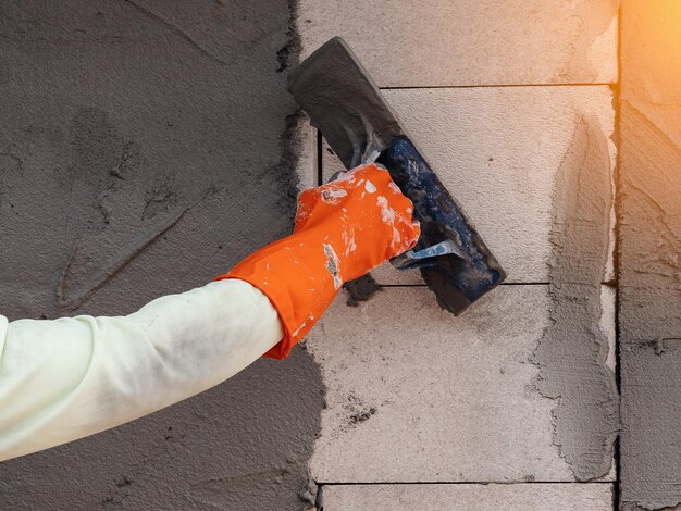 Mano tagliata di un operaio che applica cemento al muro in un cantiere