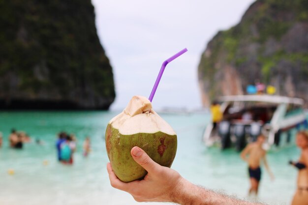 Mano tagliata di un uomo che tiene una noce di cocco sulla spiaggia