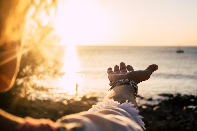Mano tagliata di una donna che fa un gesto sulla spiaggia contro il mare e il cielo durante il tramonto