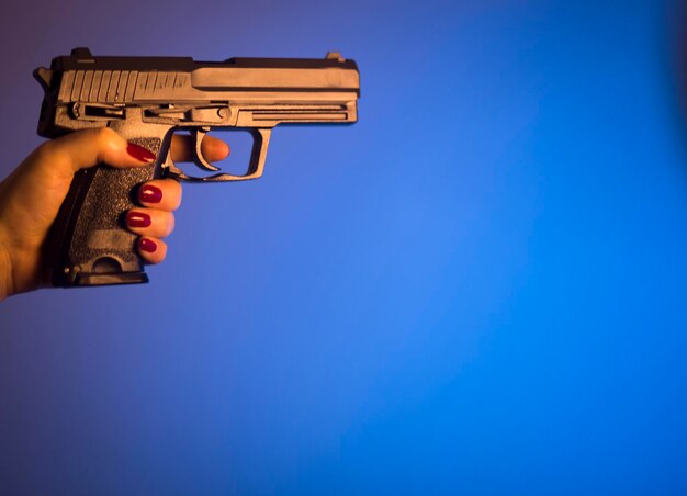 Mano tagliata di una donna che tiene una pistola contro uno sfondo blu