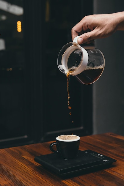 Mano tagliata di una persona che versa il caffè in una tazza sul tavolo