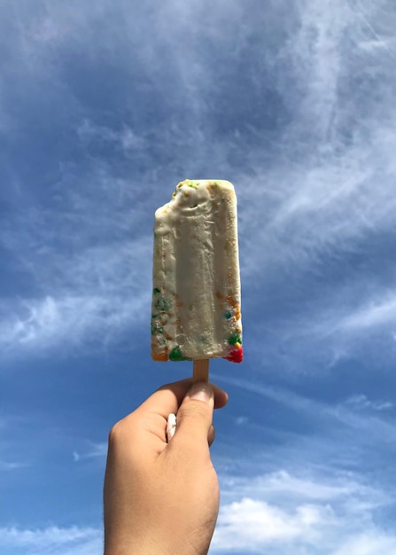 Mano umana che tiene il gelato contro il cielo