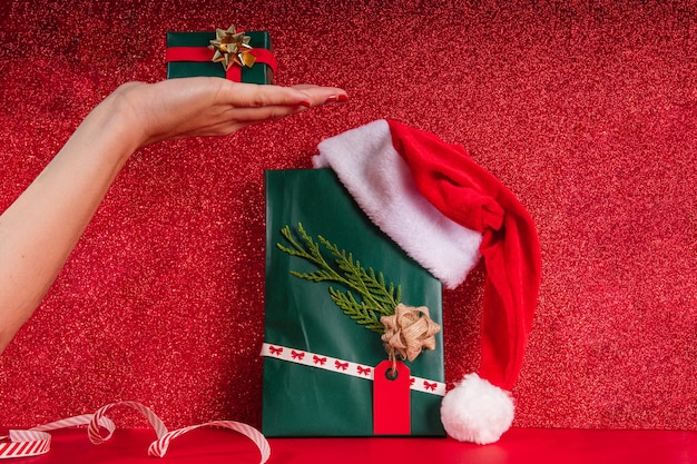 Mano umana che tiene un regalo verde sopra un regalo di natale concentrato con gli ornamenti