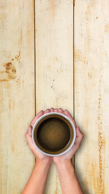 Mano umana che tiene una tazza di caffè su sfondo di legno Concetto di giornata internazionale del caffè