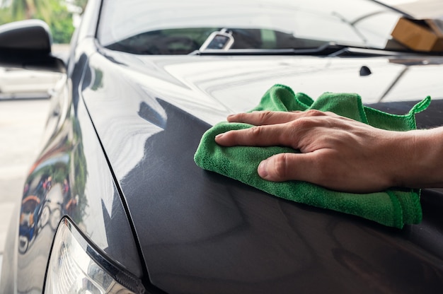 Mano uomo con panno in microfibra verde che pulisce sul cofano dell'auto grigio